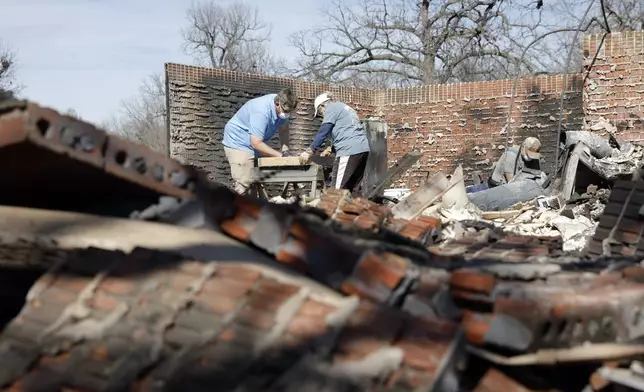 Cayton Jones, left, and his family look through the ashes of his home in the Hidden Oaks neighborhood in Stillwater, Okla., Monday, March 17, 2025, after wildfires burned through the area on Friday. (AP Photo/Alonzo Adams)