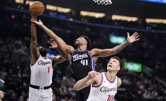 Los Angeles Clippers guard James Harden, left, grabs a rebound away from Sacramento Kings forward Trey Lyles, center, as guard Bogdan Bogdanovic watches during the first half of an NBA basketball game Sunday, March 9, 2025, in Inglewood, Calif. (AP Photo/Mark J. Terrill)