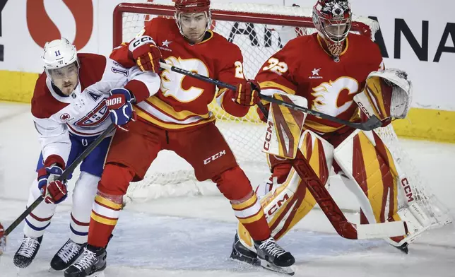 Montreal Canadiens' Brendan Gallagher, left, is checked by Calgary Flames' Jake Bean, centre, as goalie Dustin Wolf follows the play during first period NHL hockey action in Calgary on Saturday, March 8, 2025. (Jeff McIntosh/The Canadian Press via AP)