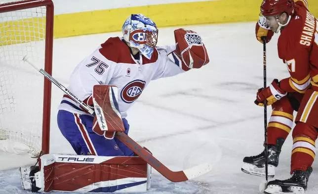 Montreal Canadiens goalie Jakub Dobes, left, grabs the puck as Calgary Flames' Yegor Sharangovich closes in during first period NHL hockey action in Calgary on Saturday, March 8, 2025. (Jeff McIntosh/The Canadian Press via AP)