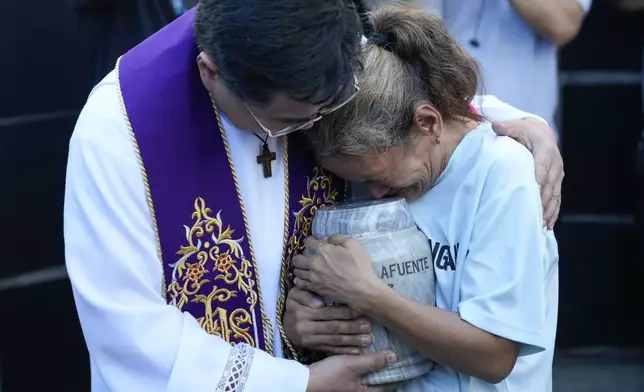 Filipino Catholic priest Flavie Villanueva, left, consoles Melinda Lafuente, as she holds the urn containing the remains of her son Angelo, during an interment ceremony for victims of extrajudicial killings, at the "Dambana ng Paghilom" or Shrine of Healing inside a cemetery in Caloocan City, Philippines, Wednesday March 12, 2025. (AP Photo/Aaron Favila)