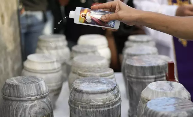 A relative sprinkles holy water on urns during an interment ceremony for victims of extrajudicial killings during the time of former President Rodrigo Duterte at the "Dambana ng Paghilom" or Shrine of Healing inside a cemetery in Caloocan City, Philippines, Wednesday, March 12, 2025. (AP Photo/Aaron Favila)