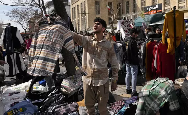 A vendor advertises clothing while people shop for the Persian new year, or Nowruz, the most important holiday for Iranians which marks the beginning of the spring, in the old main bazaar of Tehran, Iran, Tuesday, March 18, 2025. (AP Photo/Vahid Salemi)