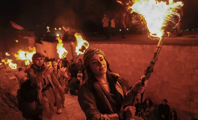 Iraqi Kurds holding lit torches walk up a mountain during a procession to celebrate their Nowruz, the Persian New Year, in Akra, Iraq, Thursday, March 20, 2025. (AP Photo/Hadi Mizban)