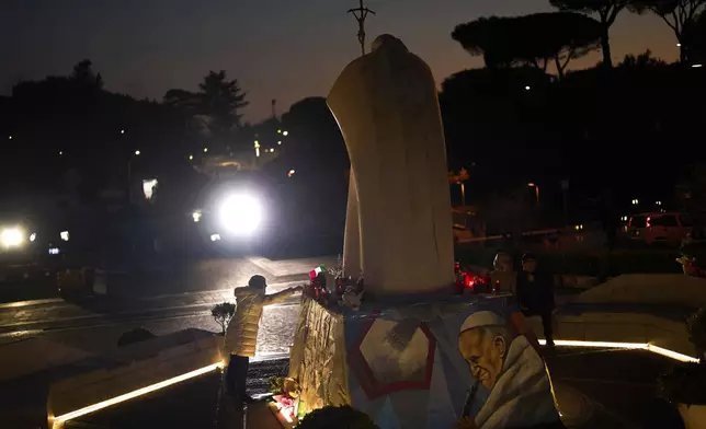 A woman touches the statue of Pope John Paul II placed outside the Agostino Gemelli hospital in Rome, Thursday, March 6, 2025. (AP Photo/Francisco Seco)