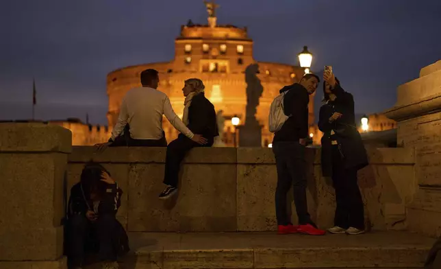 Tourists sit near Sant'Angelo castle, background, as the sun sets in Rome, Italy, Friday, March 7, 2025. (AP Photo/Francisco Seco)