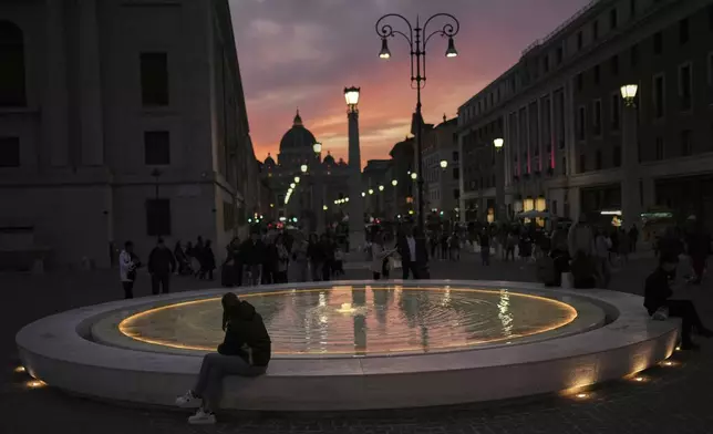 Locals and tourists walk along a main street near St. Peter's Basilica, background, as the sun sets in Rome, Italy, Friday, March 7, 2025. (AP Photo/Francisco Seco)