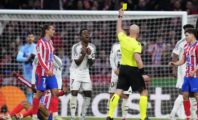 Referee Szymon Marciniak shows a yellow card to Real Madrid's Vinicius Junior during the Champions League round of 16, second leg, soccer match between Atletico Madrid and Real Madrid at the Metropolitano stadium in Madrid, Spain, Wednesday, March 12, 2025. (AP Photo/Manu Fernandez)