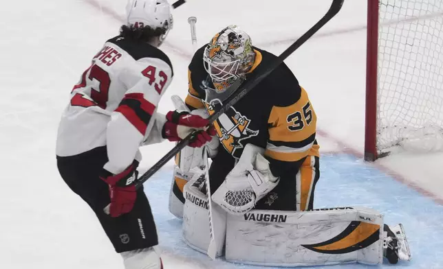 Pittsburgh Penguins goaltender Tristan Jarry (35) blocks a shot by New Jersey Devils' Luke Hughes (43) during the first period of an NHL hockey game in Pittsburgh, Saturday, March 15, 2025. (AP Photo/Gene J. Puskar)
