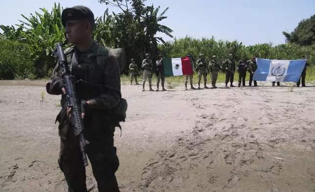 Guatemalan soldiers, right, hold up a national flag alongside Mexican soldiers, at the shared border as part of Guatemala's Ring of Fire operation, aiming to strengthen border control, at the Suchiate River in Ocos, Guatemala, Thursday, March 13, 2025. (AP Photo/Moises Castillo)