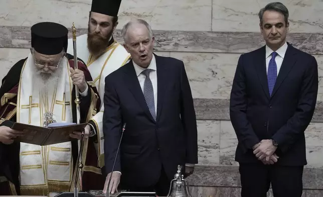 Greece's New President Constantine Tassoulas, center, takes an oath next to Archbishop of Athens and All Greece Ieronimos as Prime Minister Kyriakos Mitsotakis stands on the right during the swearing in ceremony at the Parliament, in Athens, Greece, Thursday, March 13, 2025. (AP Photo/Thanassis Stavrakis)