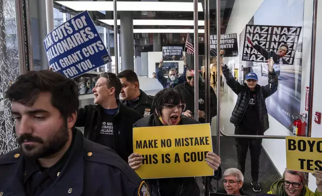 Demonstrators stand inside and in the entrance of a Tesla showroom during a protest against Elon Musk and Tesla, Saturday, March 01, 2025 in New York. (AP Photo/Adam Gray)