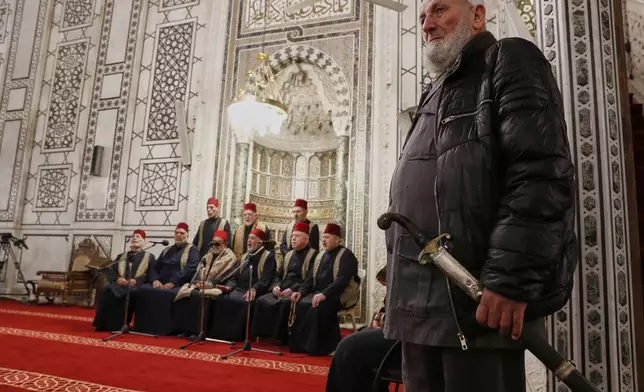 A man holds a traditional sword next to a group of sheikhs reading the Quran during the first Ramadan Friday prayer at the Umayyad mosque in Damascus, Friday, March 7, 2025.(AP Photo/Omar Sanadiki)