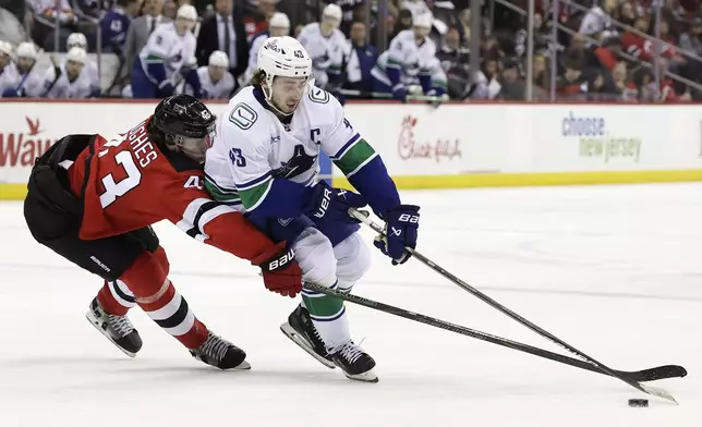 Vancouver Canucks defenseman Quinn Hughes (43) controls the puck past his brother New Jersey Devils defenseman Luke Hughes during the third period of an NHL hockey game Monday, March 24, 2025, in Newark, N.J. (AP Photo/Adam Hunger)