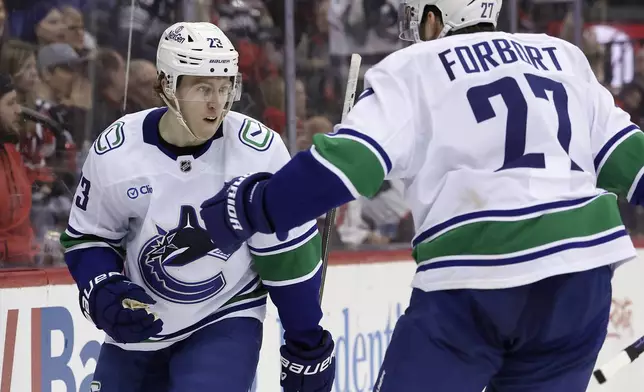 Vancouver Canucks right wing Jonathan Lekkerimaki (23) is congratulated after scoring a goal by Derek Forbort during the third period of an NHL hockey game against the New Jersey Devils Monday, March 24, 2025, in Newark, N.J. (AP Photo/Adam Hunger)