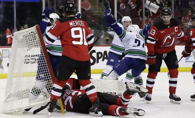 Vancouver Canucks center Pius Suter (24) reacts after scoring in front of New Jersey Devils center Nico Hischier (13) during the third period of an NHL hockey game Monday, March 24, 2025, in Newark, N.J. (AP Photo/Adam Hunger)