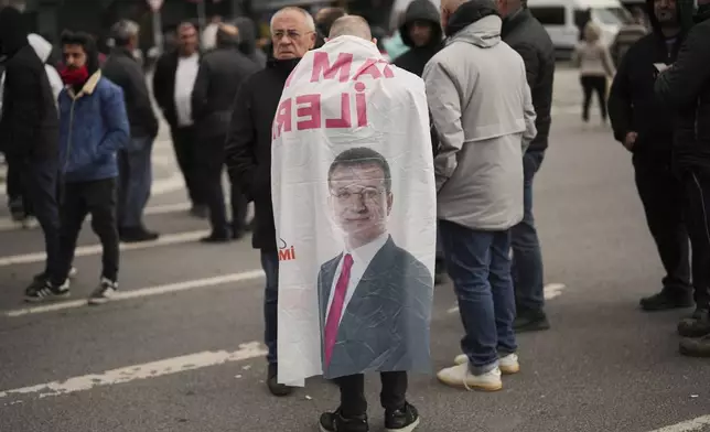 A man wears a banner featuring a photo of Istanbul Mayor Ekrem Imamoglu as he and others protest outside the Vatan Security Department, where Imamoglu is expected to be taken following his arrest in Istanbul, Turkey, Wednesday, March 19, 2025. (AP Photo/Francisco Seco)