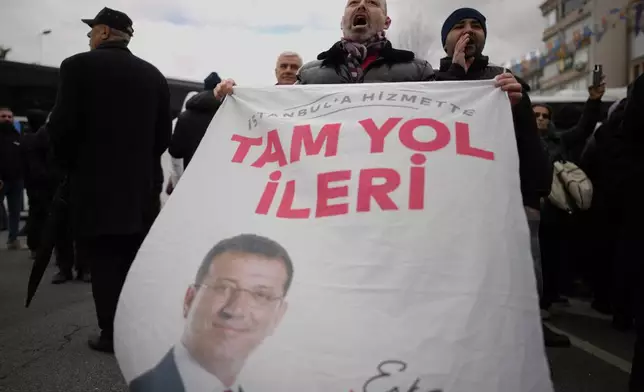 People chant slogans, one holding a banner featuring a photo of Istanbul Mayor Ekrem Imamoglu, while protesting his arrest in Istanbul, Turkey, Wednesday, March 19, 2025. (AP Photo/Emrah Gurel)