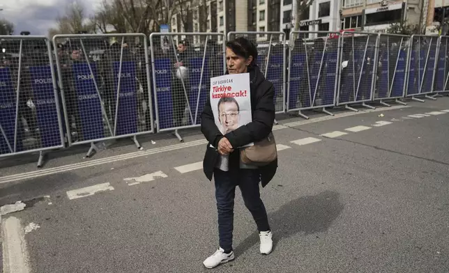 A woman protests, holding a poster of Istanbul Mayor Ekrem Imamoglu, in front of a police cordon blocking the roads leading to the Vatan Security Department, where Imamoglu is expected to be taken following his arrest in Istanbul, Turkey, Wednesday, March 19, 2025. (AP Photo/Francisco Seco)