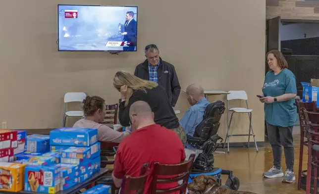 Families evacuated from wildfires near Norman, Okla. talk and watch the latest news information on tv at CrossPoint Church in Norman on Friday, March 14, 2025. (AP Photo/Alonzo Adams)