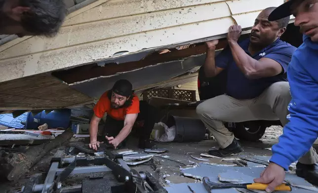 Matt Wolff, left, works underneath his carport with the help of his father-in-law Dempsey Watson and friend Tyler Umbright, right, as they work to stabilize after a severe storm in Bridgeton, Mo., Saturday, March 15, 2025. (Robert Cohen/St. Louis Post-Dispatch via AP)