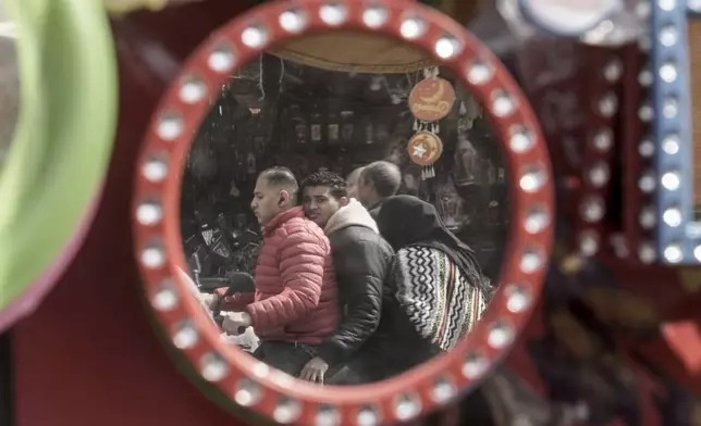 Visitors on a motor bike are reflected on Ramadan traditional decorations at a popular market marking the holy month of Ramadan, in Cairo, Egypt, Friday, March 7, 2025. (AP Photo/Amr Nabil)
