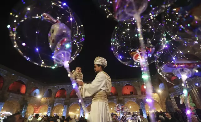 A dancer holds a baby as he performs during Ramadan festival at the historical castle of Sidon, south of Lebanon, Friday, March 7, 2025. (AP Photo/Mohammed Zaatari)