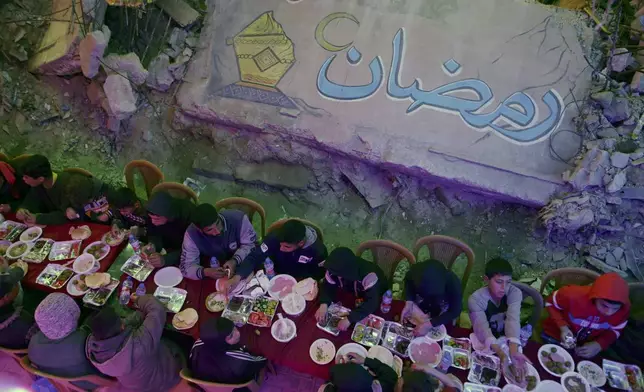 Palestinians hold a collective suhoor meal next to their destroyed homes for the holy month of Ramadan in Khan Younis, southern Gaza Strip, Friday, Feb. 28, 2025. Arabic reads: "Ramadan." (AP Photo/Jehad Alshrafi)