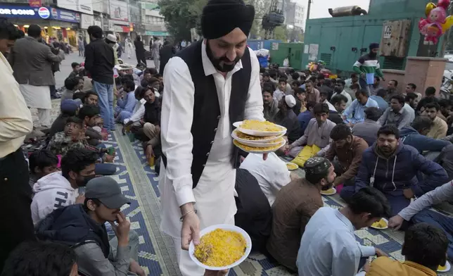 A Sikh volunteer distributes food plates among people for breaking their fast during the holy fasting month of Ramadan, at a free meal point, in Lahore, Pakistan, Monday, March 10, 2025. (AP Photo/K.M Chaudary)