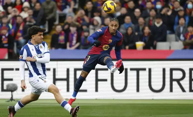 Barcelona's Raphinha, right, passes the ball challenged by Real Sociedad's Jon Aramburu during the Spanish La Liga soccer match between Barcelona and Real Sociedad at the Lluis Companys Olympic Stadium in Barcelona, Spain, Sunday, March 2, 2025. (AP Photo/Joan Monfort)