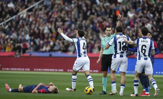 Referee Alejandro Quintero Gonzalez shows a red card to Real Sociedad's Aritz Elustondo (6) as Barcelona's Dani Olmo lies on the pitch during the Spanish La Liga soccer match between Barcelona and Real Sociedad at the Lluis Companys Olympic Stadium in Barcelona, Spain, Sunday, March 2, 2025. (AP Photo/Joan Monfort)
