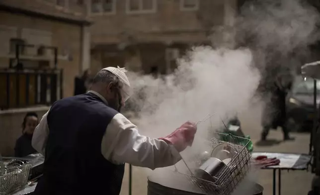 An ultra-Orthodox Jewish man dips cooking utensils in boiling water to remove remains of leaven in preparation for the upcoming Jewish holiday of Passover, in the ultra-Orthodox neighbourhood Mea Shearim, in Jerusalem, Thursday, April 10, 2025. (AP Photo/Leo Correa)