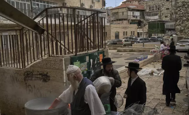 An ultra-Orthodox Jewish man dips cooking utensils in boiling water to remove remains of leaven, in preparation for the upcoming Jewish holiday of Passover, in the ultra-Orthodox neighbourhood Mea Shearim, in Jerusalem, Thursday, April 10, 2025. (AP Photo/Leo Correa)