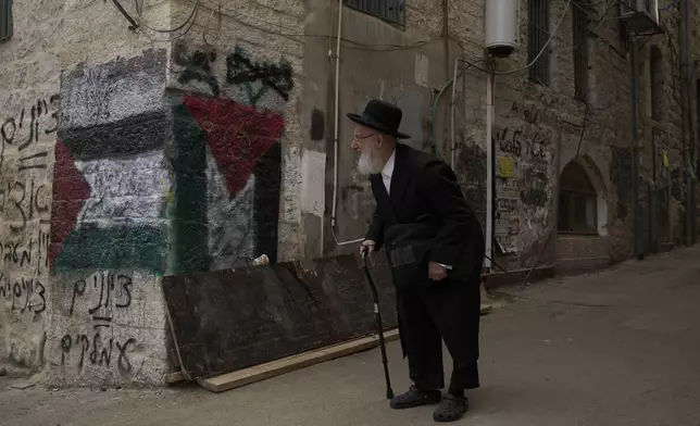 An ultra-Orthodox Jew walks past walls with paintings depicting Palestinians flags, in an alley in the the ultra-Orthodox neighborhood Mea Shearim, ahead of the upcoming Jewish holiday of Passover, in Jerusalem, Thursday, April 10, 2025. (AP Photo/Leo Correa)