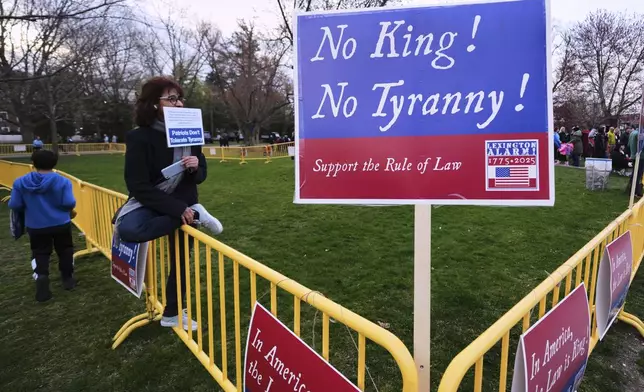 A lone protestor sits in the "Free Speech Zone" during a reenactment celebration of the 250th anniversary of the Battle of Lexington and start of the American Revolution, Saturday, April 19, 2025, in Lexington, Mass. (AP Photo/Charles Krupa)