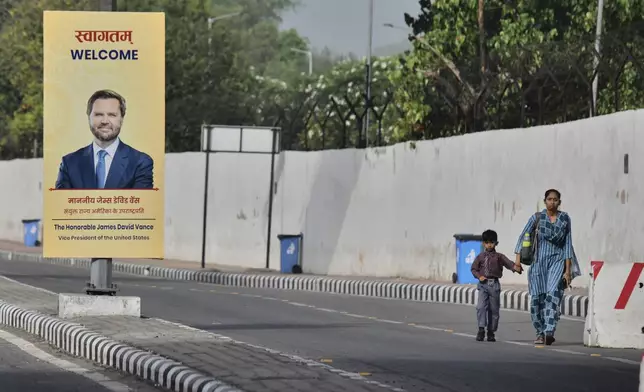 A woman and a child walk past a banner welcoming U.S. Vice President JD Vance on a street in New Delhi, India, Monday, April 21, 2025. (AP Photo)