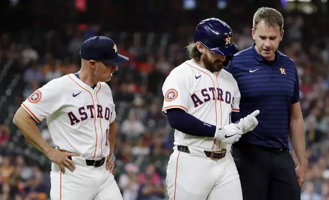 Houston Astros' Brendan Rodgers, center, looks at his hand as he is escorted to first base by manager Joe Espada, left, and an unidentified trainer, right, after Rodgers was hit by a pitch from Toronto Blue Jays starting pitcher Chris Bassitt during the third inning of a baseball game Tuesday, April 22, 2025, in Houston. (AP Photo/Michael Wyke)