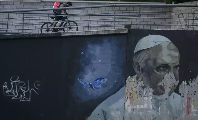 FILE - A man rides a bicycle near a weathered mural of Pope Francis in Buenos Aires, Argentina, March 2, 2023. (AP Photo/Natacha Pisarenko, File)