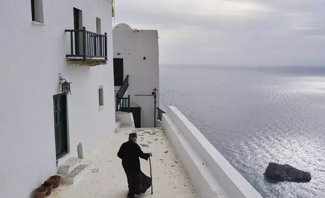 Orthodox Christian monk Father Spyridon walks at the Monastery of Panagia Hozoviotissa as the Aegean Sea is seen on the right, in Amorgos island, Greece, on Wednesday March 27, 2025. (AP Photo/Petros Giannakouris)