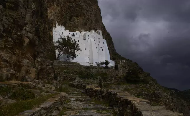 The Monastery of Panagia Hozoviotissa, carved into a cliffside high above the Aegean Sea is illuminated by the sun during a cloudy day, in Amorgos island, Greece, on Sunday, March 30, 2025. (AP Photo/Petros Giannakouris)