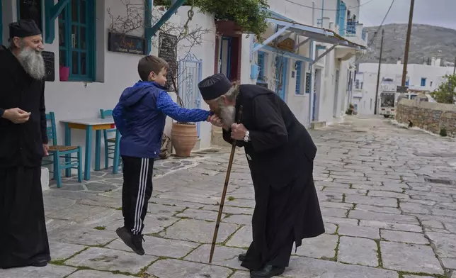 Orthodox Christian monk Father Spyridon of Amorgos, kisses the hand of the son of his nephew Nikitas Vasalos as father Kostas looks on, in Lagada village, Amorgos island, Greece, on Saturday, March 29, 2025.(AP Photo/Petros Giannakouris)