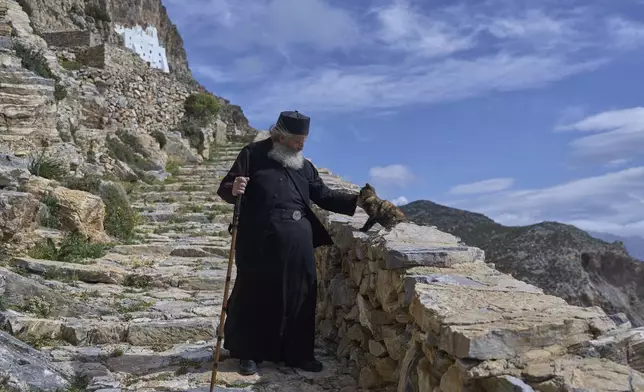 Orthodox Christian monk Father Spyridon of Amorgos pets a cat as he leaves the Monastery of Panagia Hozoviotissa, seen in the background, in Amorgos Island, Greece, on Sunday, March 30, 2025. (AP Photo/Petros Giannakouris)