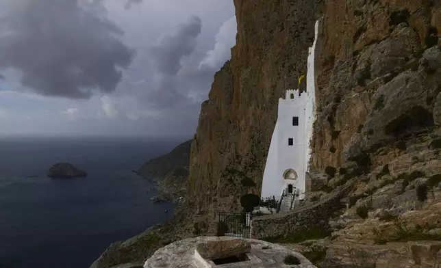 The Monastery of Panagia Hozoviotissa, carved into a cliffside high above the Aegean Sea is illuminated by the sun during a cloudy day, in Amorgos island, Greece, on Saturday, March 29, 2025. (AP Photo/Petros Giannakouris)