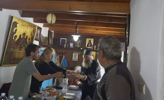 From left, Constantin Papakonstantinou, an assistant residing at the monastery, Ioanna Kape, Head of the Amorgos Port Authority, and Christian Orthodox monk Father Spyridon of Amorgos, as dinner is served at the Monastery of Panagia Hozoviotissa on Thursday, March 27, 2025. (AP Photo/Petros Giannakouris)