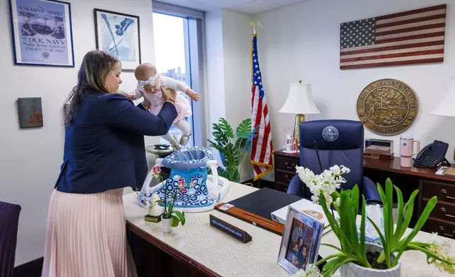 Florida Rep. Fiona McFarland, R-Sarasota, lifts her 7-month-old daughter Grace Melton into a chair on her desk as she starts her work day at the state Capitol, Thursday, April 17, 2025, in Tallahassee, Fla. (AP Photo/Colin Hackley)