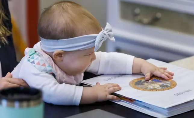 Grace Melton, 7-month-old, is held by her mother, Florida Rep. Fiona McFarland, R-Sarasota, while she touches a binder on her desk, Thursday, April 17, 2025, in Tallahassee, Fla. (AP Photo/Colin Hackley)
