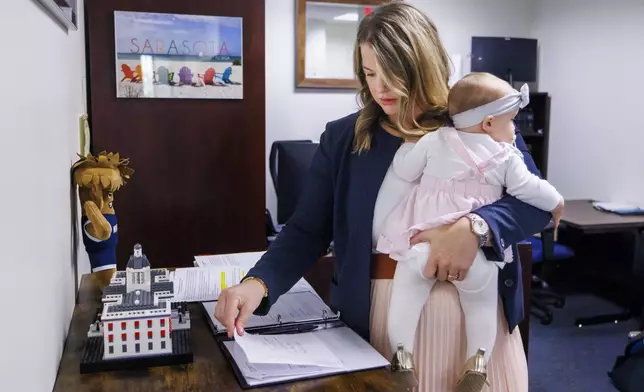 Florida Rep. Fiona McFarland, R-Sarasota, reviews a bill before committee while holding her 7-month-old daughter Grace Melton, Thursday, April 17, 2025, in Tallahassee, Fla. (AP Photo/Colin Hackley)