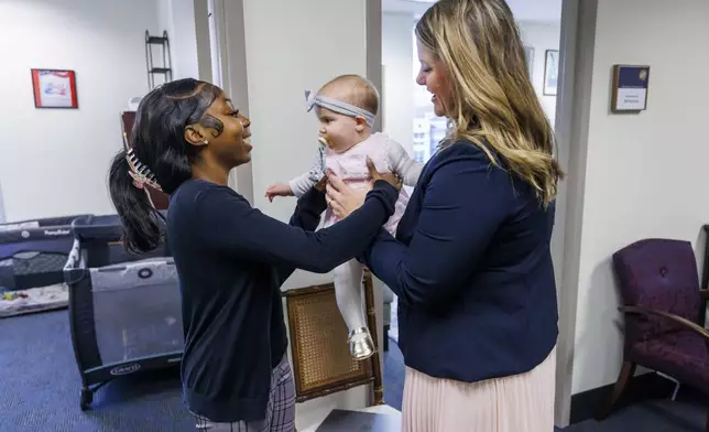 Florida Rep. Fiona McFarland, R-Sarasota, right, hands 7-month-old daughter Grace Melton to Mycah Moore, a childcare worker who helps McFarland, as she leaves her office for a committee hearing, Thursday, April 17, 2025, in Tallahassee, Fla. (AP Photo/Colin Hackley)