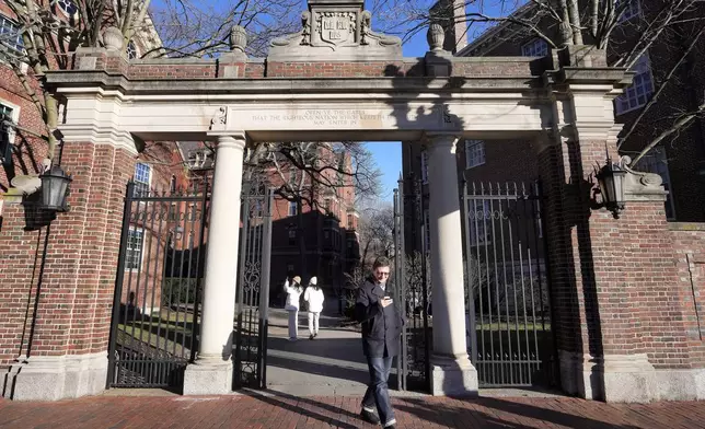 A passer-by walks through a gate to the Harvard University campus, Tuesday, Jan. 2, 2024, in Cambridge, Mass. Harvard University President Claudine Gay resigned Tuesday amid plagiarism accusations and criticism over testimony at a congressional hearing where she was unable to say unequivocally that calls on campus for the genocide of Jews would violate the school's conduct policy. (AP Photo/Steven Senne)
