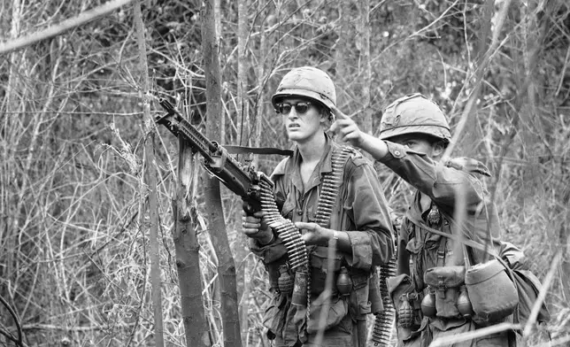 FILE- Infantryman points out a suspicious shadow in a tree to his machine gunner as they move on patrol near the Cambodian Border west of Pleiku in Vietnam on Nov. 26, 1966. Troops of the 25th Infantry Division (1st Battn. 14th Inf.) inches through the thick jungle from their base camp after being held up three days by snipers. AP Photo/Horst Faas, File)